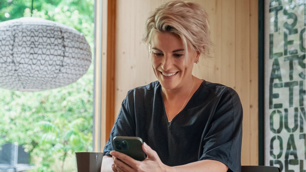 Foto av smilende kvinne som ser på mobilen.