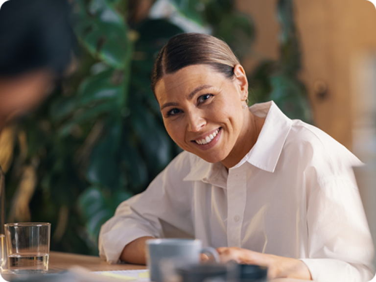 Photo of a smiling woman seated at a desk in a modern open-plan office.